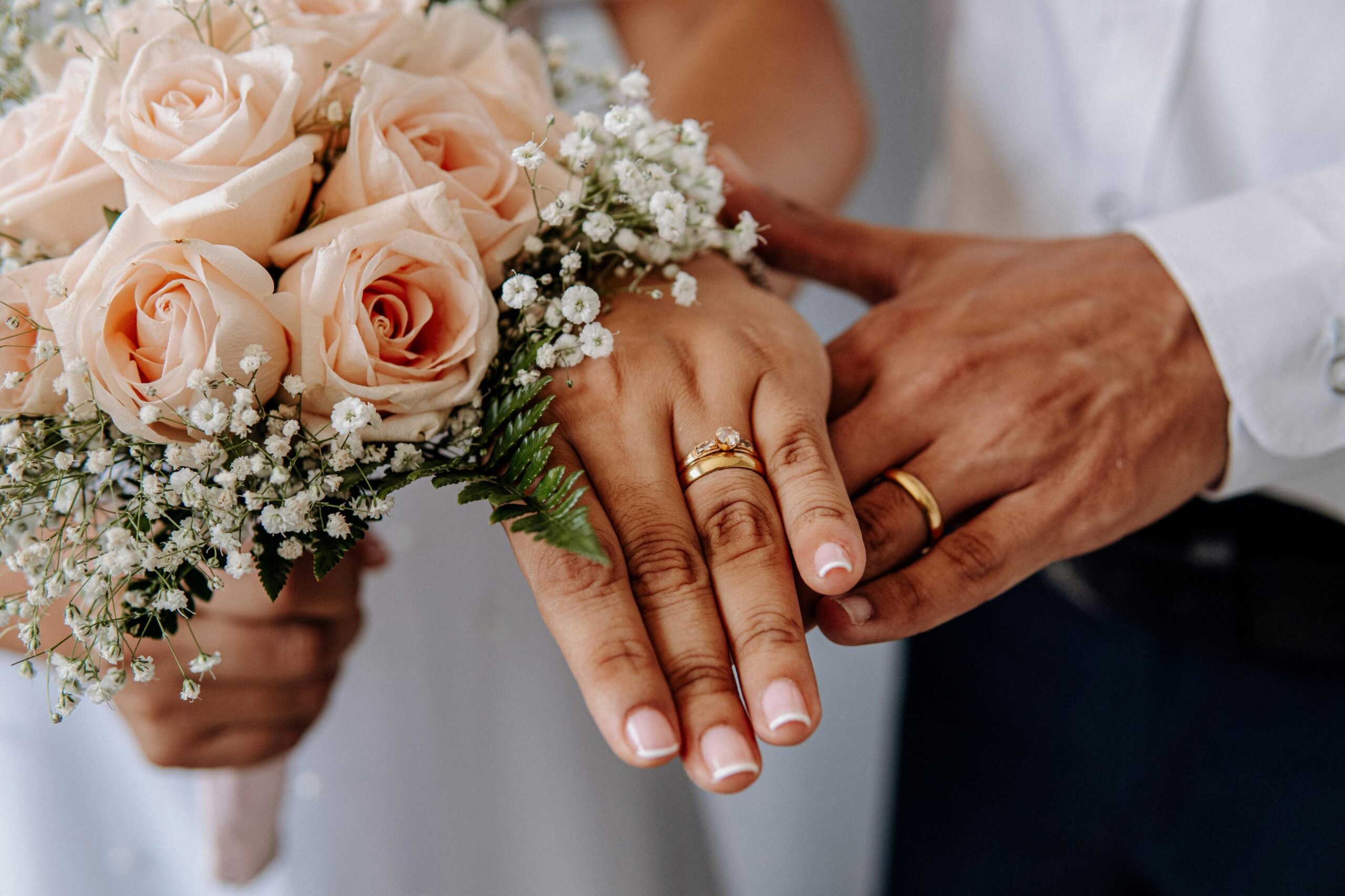 Close-up of wedding rings on couple's hands with rose bouquet, symbolizing love and commitment.