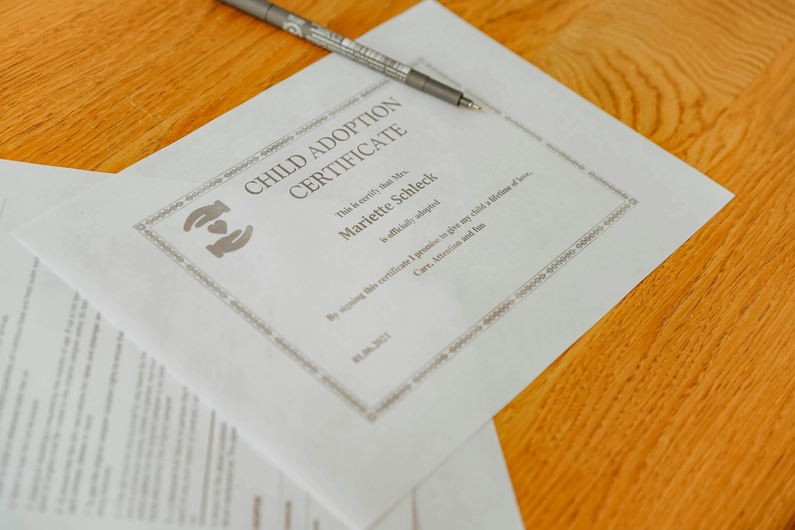 Close-up of a child adoption certificate and documents with a pen on a wooden table.